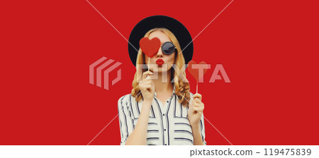 Portrait of beautiful young woman blowing her lips sends kiss with sweet red heart shaped lollipop Portrait of beautiful young woman blowing her lips sends kiss with sweet red heart shaped lollipop 119475839