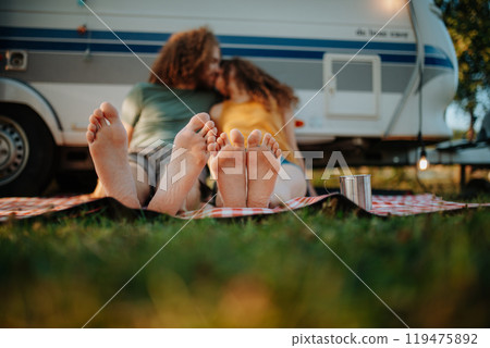Couple sitting by caravan and kissing, enjoying cup of morning coffee outdoors. Camping trip for young people. Couple sitting by caravan and kissing, enjoying cup of morning coffee outdoors. Camping trip for young people. 119475892