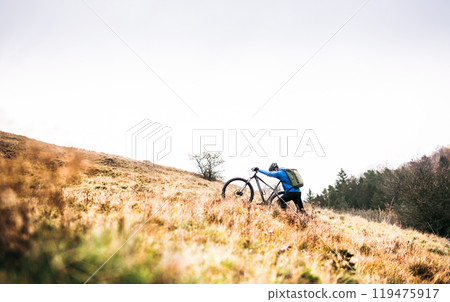 Man pushing his bike up the hill in the middle of beautiful nature, enjoying beautiful view. Concept of healthy lifestyle. Man pushing his bike up the hill in the middle of beautiful nature, enjoying beautiful view. Concept of healthy lifestyle. 119475917