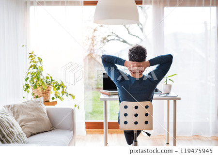 Homeoffice for handsome man. Rear view of man sitting on office chair with hands behind head, working at desk from home. Telecommuting. Homeoffice for handsome man. Rear view of man sitting on office chair with hands behind head, working at desk from home. Telecommuting. 119475945