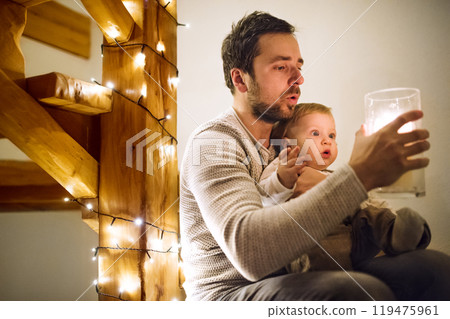 Little baby boy with father looking at decorated Christmas home. Cute boy is surprised and amazed by the Christmas magic. Little baby boy with father looking at decorated Christmas home. Cute boy is surprised and amazed by the Christmas magic. 119475961