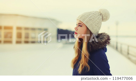Portrait of beautiful blonde young woman posing in winter hat outdoors 119477006
