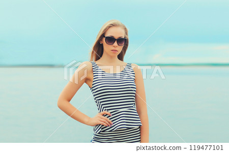 Beautiful young woman posing in sunglasses, striped dress on sea coast 119477101