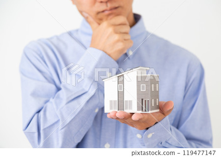 A middle-aged man holding a house model and worrying 119477147
