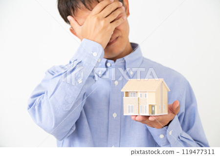 一名中年男子拿著房屋模型,憂心忡忡 一名中年男子拿著房屋模型,憂心忡忡 119477311