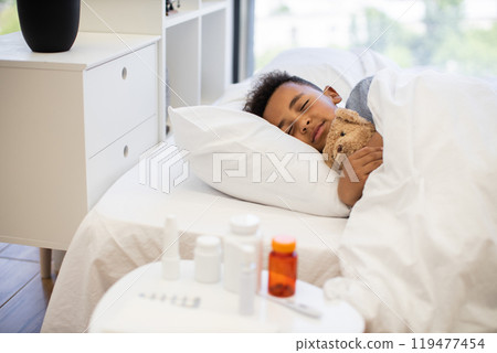 Comforting scene of a sick African boy resting in bed Comforting scene of a sick African boy resting in bed 119477454