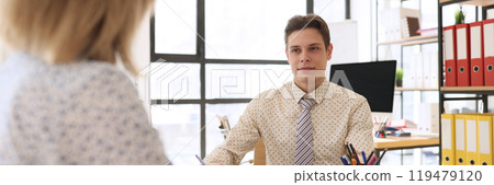 Young economist looks at woman sitting at table by clipboard 119479120