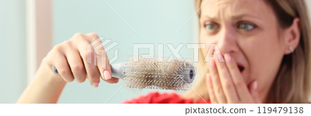Scared woman holds hairbrush with fallen hair in hand Scared woman holds hairbrush with fallen hair in hand 119479138