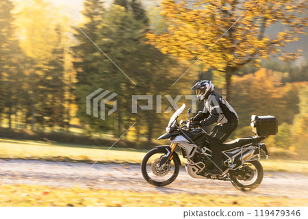 Motorcyclist rides through scenic autumn forest trail. 119479346