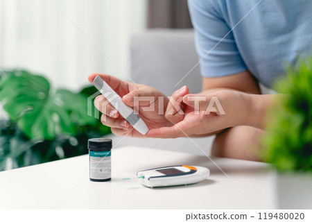Asian woman using lancet on finger for checking blood sugar level by Glucose meter 119480020