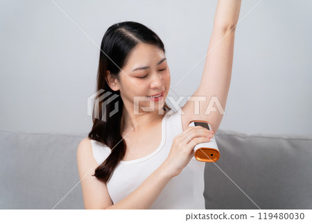 A beautiful woman is epilating her armpits using an IPL laser hair removal epilator device A beautiful woman is epilating her armpits using an IPL laser hair removal epilator device 119480030