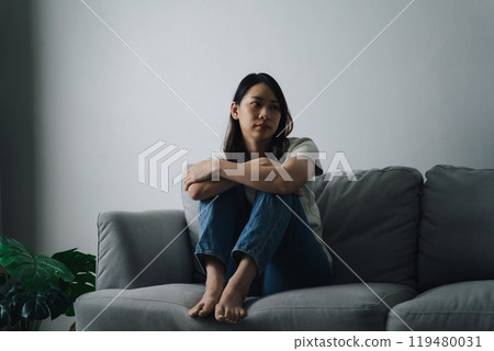 Unhappy lonely depressed woman is sitting on the couch. She looks sad and tired. Unhappy lonely depressed woman is sitting on the couch. She looks sad and tired. 119480031