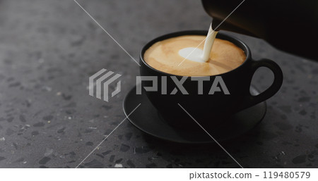 pouring steamed milk into cappuccino in black cup on terrazzo countertop pouring steamed milk into cappuccino in black cup on terrazzo countertop 119480579