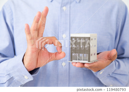 A middle-aged man making a circle sign while holding a model of a building 119480793