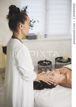 Face massage in professional salon. Therapist working with woman laying on back, vertical format, selective focus. 119480808
