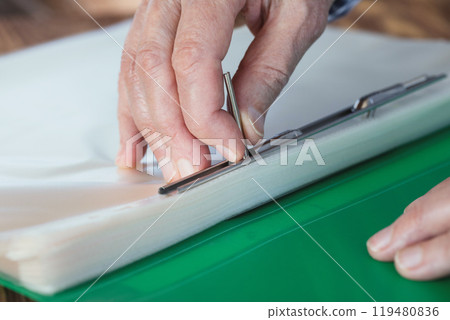Elderly female hands with green plastic file folder, person pulls out files, close-up, macro, selective focus. 119480836