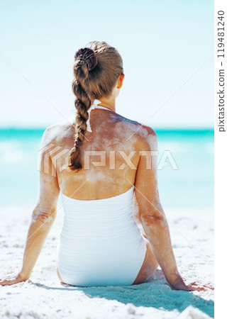 Young woman in swimsuit sitting on sandy beach . rear view 119481240