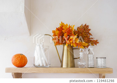Autumn decor with vibrant leaves and pumpkins on a wooden shelf on white plaster wall background 119481298