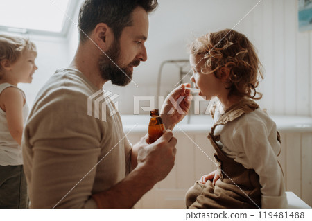 Sick girl with fever and cold at home. Father giving his daughter medicine on spoon, cough syrup or fever medicine. Sick girl with fever and cold at home. Father giving his daughter medicine on spoon, cough syrup or fever medicine. 119481488