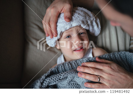 Father taking care of sick son with fever and cold, holdig cold cloth to his forehead. Boy lying on sofa, feeling tired. Top view. Father taking care of sick son with fever and cold, holdig cold cloth to his forehead. Boy lying on sofa, feeling tired. Top view. 119481492