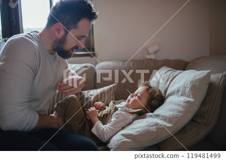 Father taking care of sick girl with fever and cold at home. Daughter lying on sofa, feeling tired. Father taking care of sick girl with fever and cold at home. Daughter lying on sofa, feeling tired. 119481499