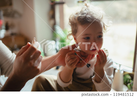 Sick girl with cold at home has stuffy nose. Father helping little daughter to breath better, using nasal spray in his nose. 119481512