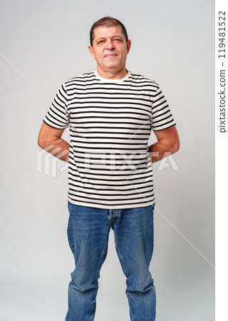 A man stands confidently in a striped shirt, casual jeans with a neutral background 119481522