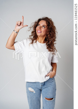 A young woman with curly hair playfully pointing finger while standing against a gray background A young woman with curly hair playfully pointing finger while standing against a gray background 119481525