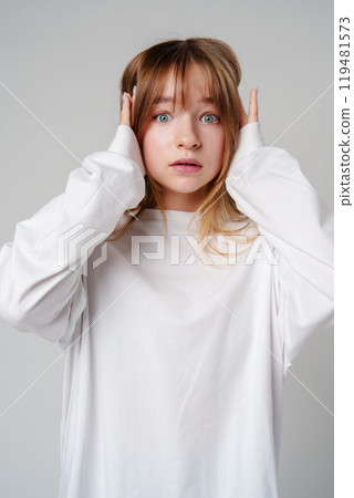 A young woman with light brown hair and blue eyes expresses surprise in a minimalist studio A young woman with light brown hair and blue eyes expresses surprise in a minimalist studio 119481573