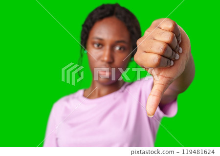 Young woman expressing disapproval with a thumbs down gesture against a bright green background 119481624