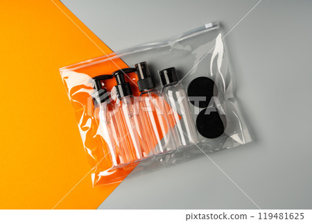 Travel-sized containers arranged neatly in a clear bag on a contrasting orange and gray background 119481625