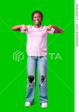 Smiling young woman pointing downwards against a bright green background Smiling young woman pointing downwards against a bright green background 119481645