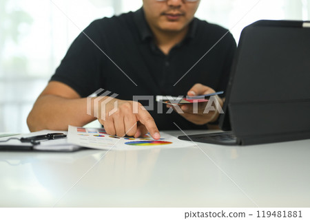 Young creative man working on a design project reviewing color chart and using laptop at desk Young creative man working on a design project reviewing color chart and using laptop at desk 119481881