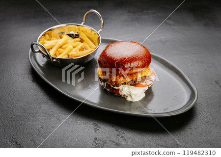 Juicy cheeseburger with crispy fries on black plate, meal for fast food lovers and comfort seekers Juicy cheeseburger with crispy fries on black plate, meal for fast food lovers and comfort seekers 119482310