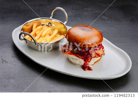 Gourmet burger with crispy bacon, raspberry sauce, and fries for an indulgent meal experience 119482313