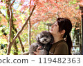一個女人和她的玩具貴賓犬一起享受秋天的落葉 秋天的風景。 119482363