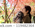 一個女人和她的玩具貴賓犬一起享受秋天的落葉 秋天的風景。 119482364
