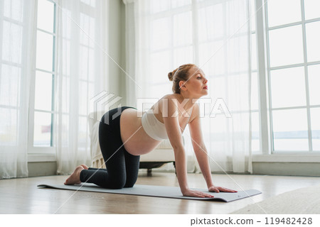 Pregnancy yoga fitness workout training. Pregnant woman practicing yoga at home. Pregnant girl doing sports exercise on yoga mat indoor. Woman with big belly have fitness training practicing asana 119482428