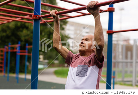 Sportive old man doing pull-ups outdoors 119483179