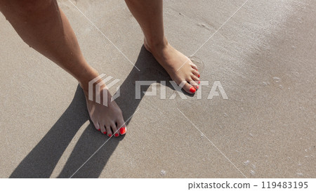 Female feet on beach sand. Woman's feet with red nails on seashore sand background in sunlight near sea. Female feet on beach sand. Woman's feet with red nails on seashore sand background in sunlight near sea. 119483195