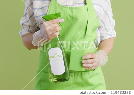 Modern woman in green apron and rubber gloves against green Modern woman in green apron and rubber gloves against green 119483228
