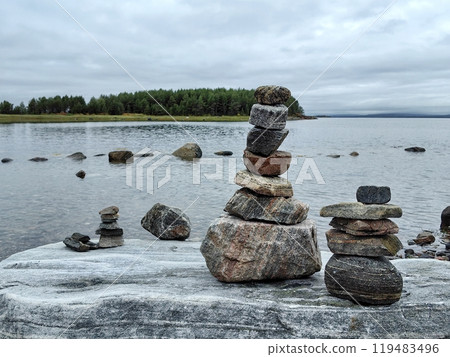 Stacked stones on a shoreline at a serene lake with cloudy skies and distant forest in late afternoon 119483496