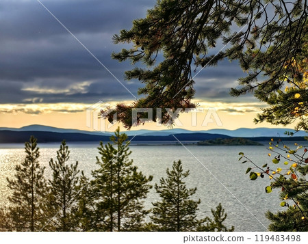 Calm lake view at sunset with trees and distant mountains in the background 119483498