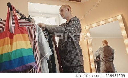 Attractive transgender man trying on female shirt and looking at mirror at home 119483569