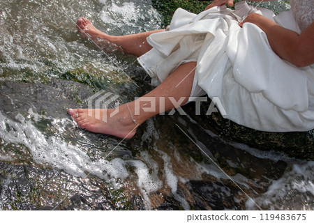 A serene bride relaxes by tranquil water in a beautiful gown, enhancing her joyful day 119483675