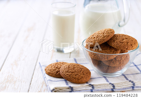 Glass and a jug of fresh milk with oatmeal cookies on a on a white table,selective focus. 119484228
