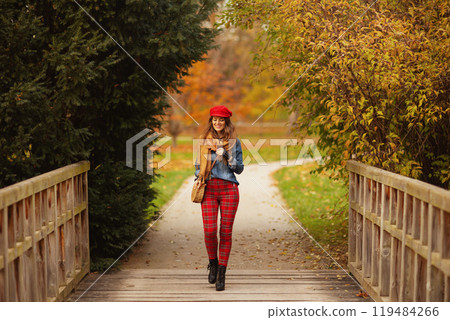smiling elegant female in jeans shirt and red hat walking 119484266
