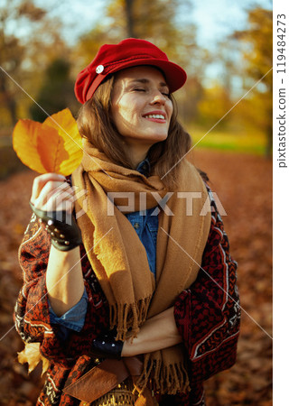 relaxed modern woman in red hat with autumn leafs and scarf 119484273
