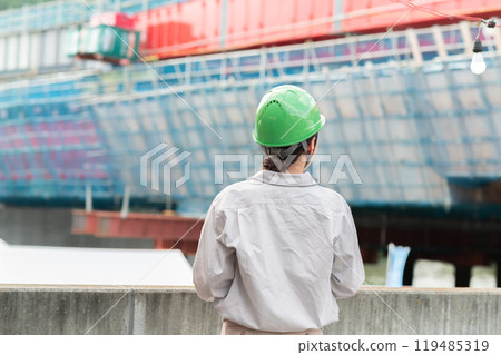 A woman in work clothes and a helmet looks at a bridge under construction 119485319