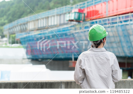 A woman in work clothes and a helmet looks at a bridge under construction 119485322